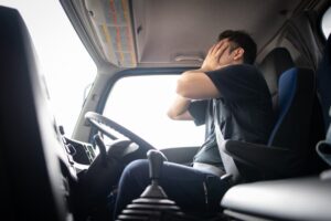 Man sitting in a truck with hands covering his face in distress.