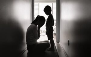 Silhouetted woman kneeling and crying with a child standing in a hallway.