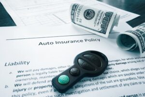 Auto insurance policy document with rolled-up money and a car key on top.