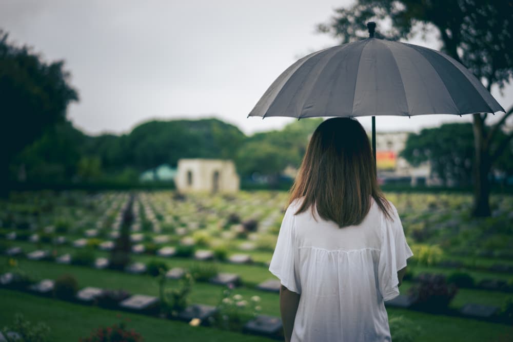 Person holding an umbrella while standing in a cemetery, viewed from behind.