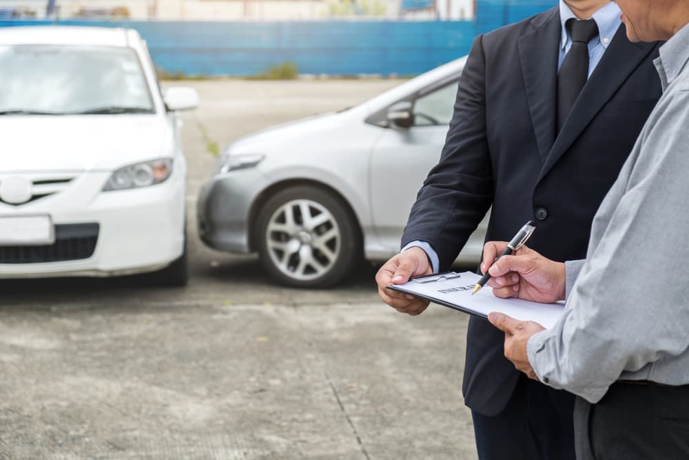 Two men reviewing and signing documents in front of cars after an accident.