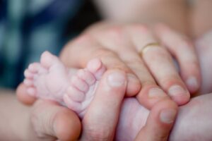 Adult hands gently holding a newborn's feet, showing care and tenderness.