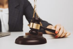 Person holding a gavel with scales of justice on a desk nearby.