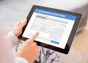 Person submitting an insurance claim using a tablet, form on screen.