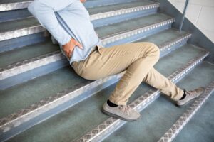 Man in casual attire clutching lower back in pain after slipping on metal stairs.