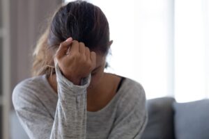 A woman sitting on a couch, holding her head in distress with her hand.