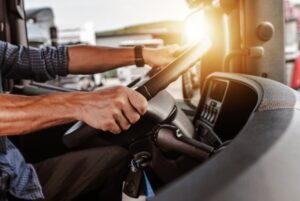 Close-up of a truck driver's hands on the steering wheel, driving in sunlight, emphasizing focus and responsibility.