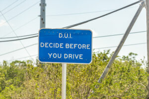 Road sign reading "D.U.I. DECIDE BEFORE YOU DRIVE" against a clear sky, promoting responsible choices to prevent driving impaired.