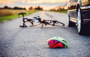 A bike lies on the road near a car with a helmet in the foreground.