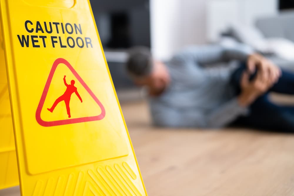 Yellow "Caution Wet Floor" sign with a person lying on the floor injured.