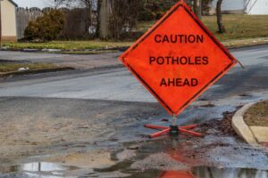 An orange road sign that reads "Caution Potholes Ahead" placed on a residential street.