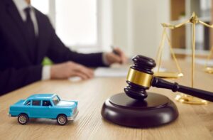 A gavel, a toy car, and scales of justice on a desk with a lawyer writing.