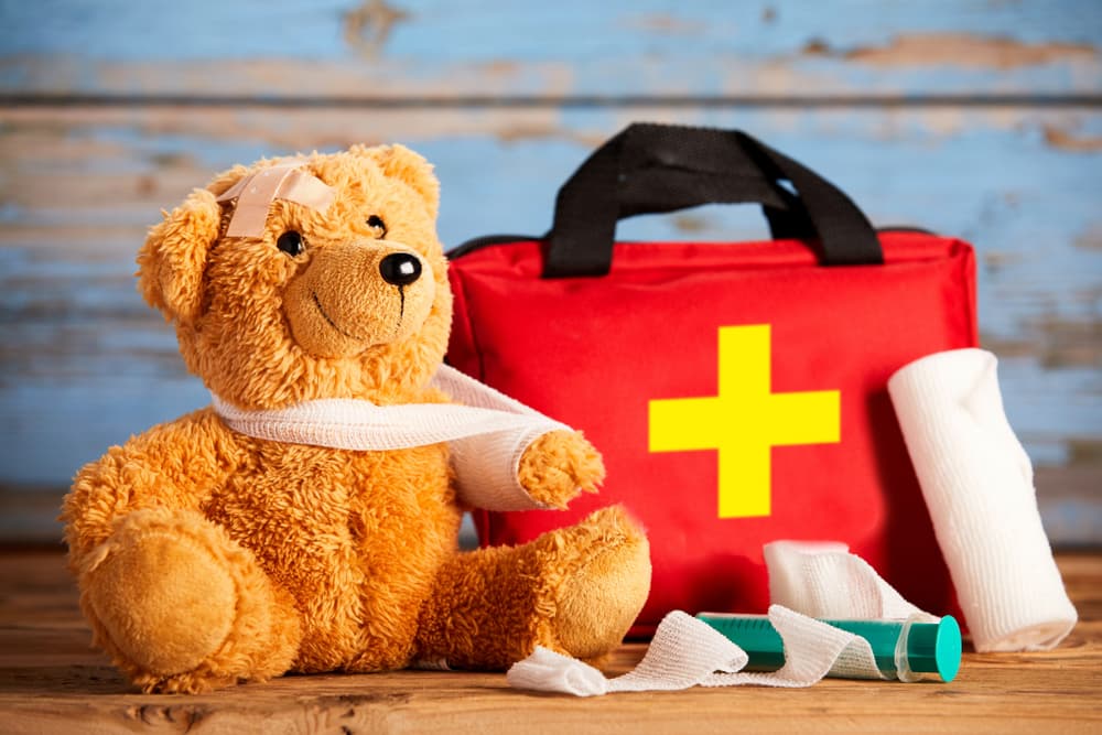 Teddy bear with bandages and a first aid kit, symbolizing pediatric injury care and prevention.