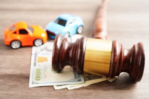 A gavel on top of money, with toy cars in the background, symbolizing car accident claims.