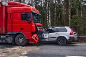 Red truck collided with a white car on a forest road, showcasing significant vehicle damage.