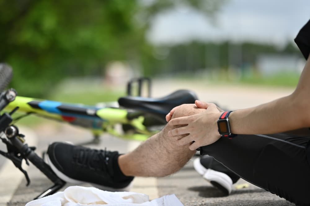 Male cyclist having an accident, falling down from bicycle and injured his knee.