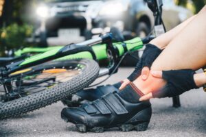 cyclist woman suffering from ankle pain after car accident on the road.