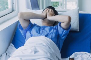 young injured man in hospital room sitting alone in pain looking negative and worried for his bad health condition